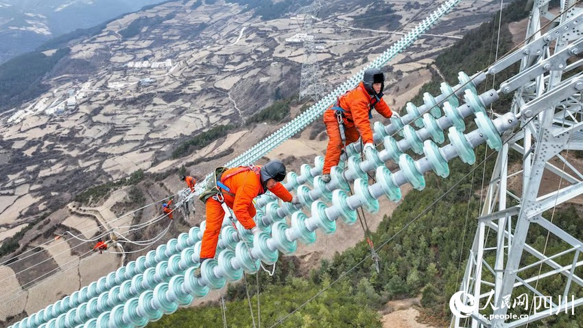 2022年1月23日，在海拔2600多米的四川大凉山腹地，凉山彝族自治州美姑县合姑洛乡合姑洛村，白鹤滩—江苏±800千伏特高压直流输电工程川1标段放线施工现场，来自国网四川电力送变电建设有限公司的电力工人曾坤银和胡志伟正在攀爬绝缘子。卢忠东摄